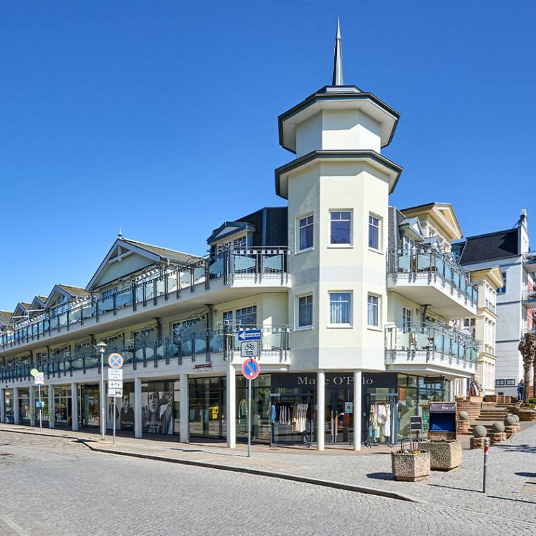 Eckansicht des Strandhotels Luise mit Balkonen und Geschäften darunter, gelegen an einer sonnigen Promenade.