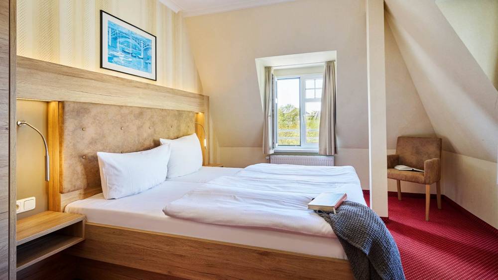 Großzügiges Doppelzimmer mit Sessel, Bett und Fenster im Strandhotel Kormoran auf Usedom.