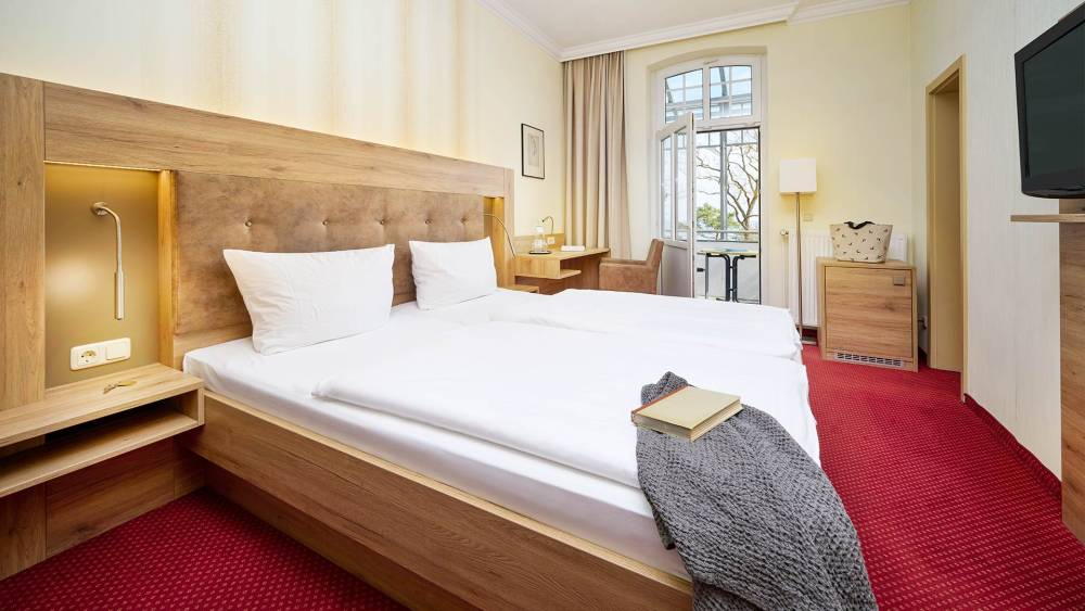 Doppelzimmer mit Bett, TV, Schreibtisch, Sessel und Fenster mit Ostseeblick.