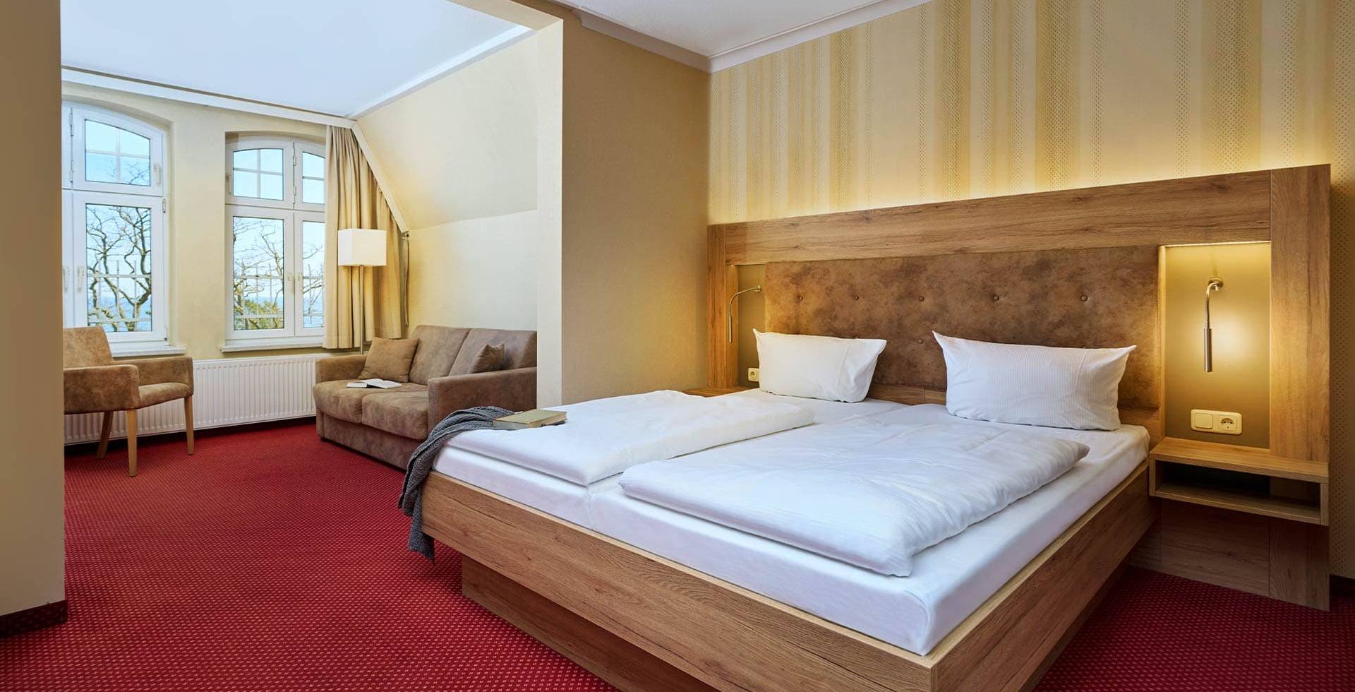 Gemütliches Doppelzimmer mit Sitzbereich und großen Fenstern im Strandhotel Garni Kormoran an der Ostsee.