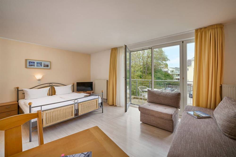 Moderne Einrichtung eines Zimmers im Appartement-Hotel Haus Strandperle mit Sofa, Doppelbett und Balkon.