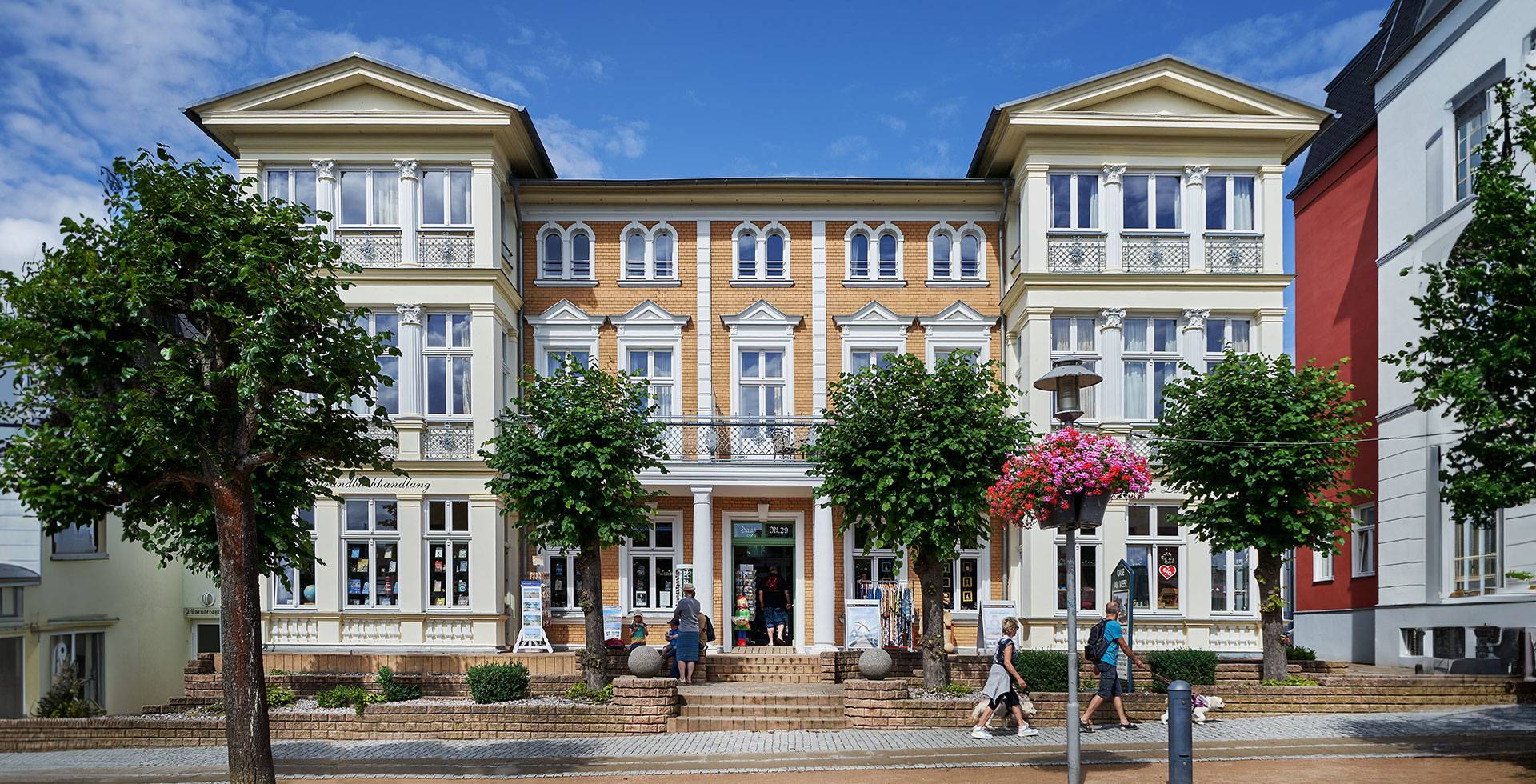 Frontansicht der Strandvilla Viktoria mit symmetrischer Architektur, großen Fenstern und Bäumen vor blauem Himmel.