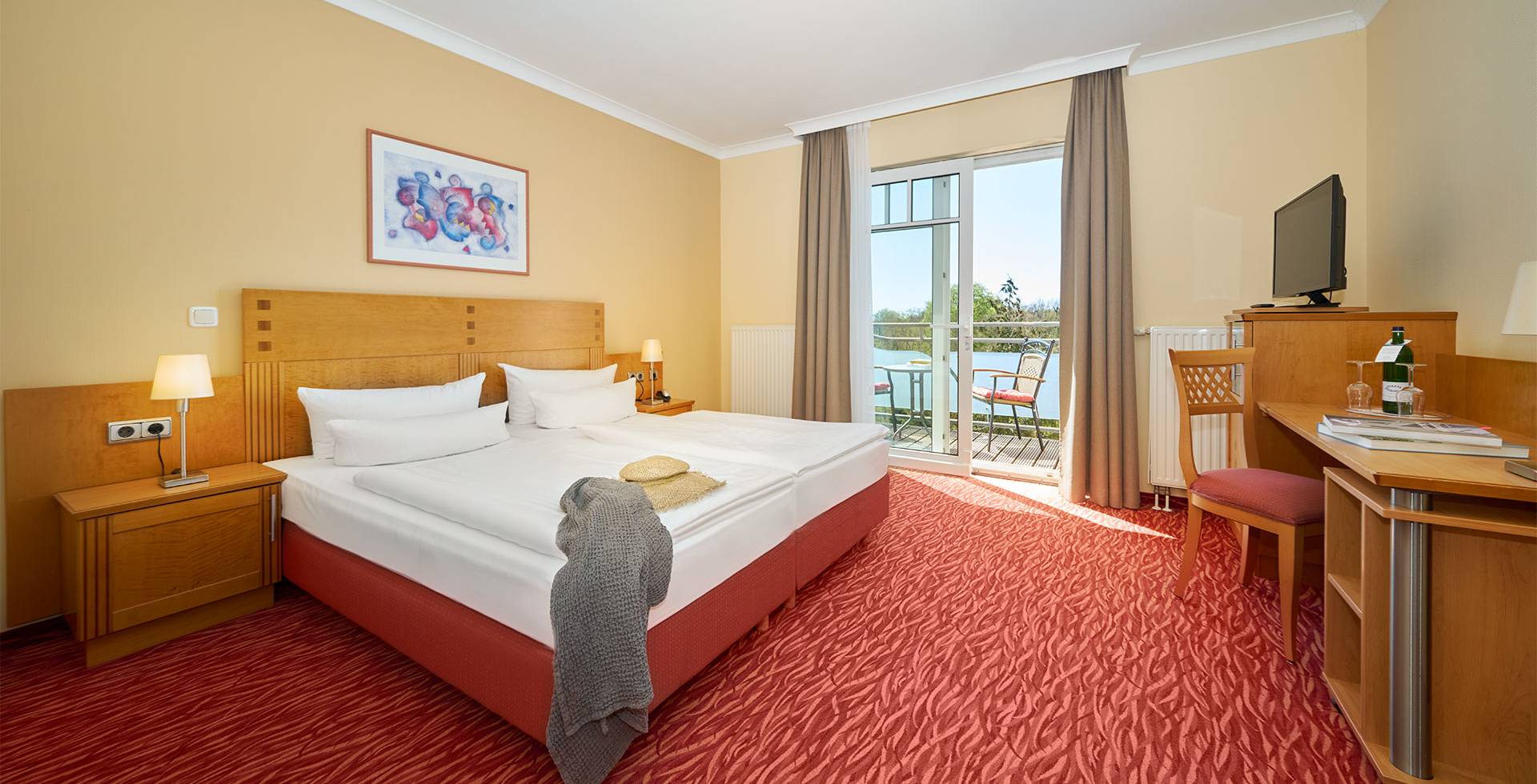Hotelzimmers mit Doppelbett, Schreibtisch, Balkon, Sesseln und Ausblick auf die Landseite im Strandhotel Prinze von Preussen.