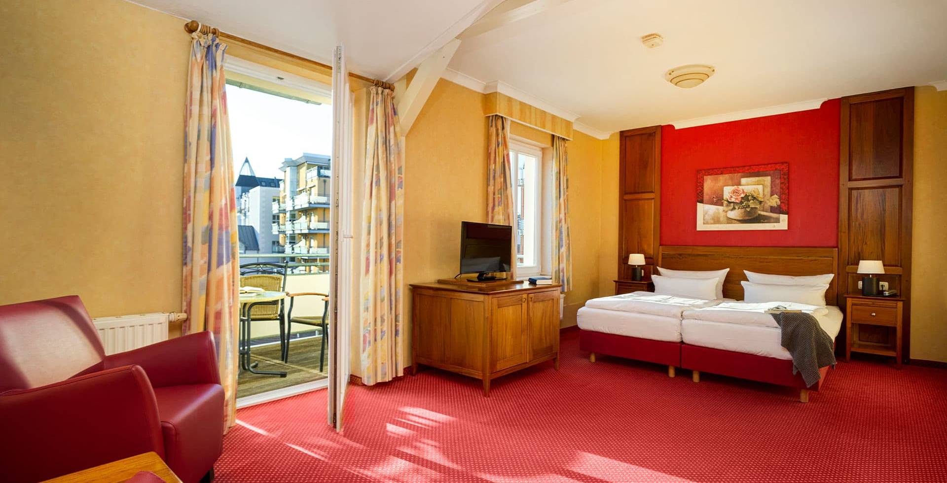 Doppelzimmer Landseite in der Strandvilla Viktoria auf Usedom mit Balkonzugang, zwei Betten, Sessel, TV und hellem Tageslicht.