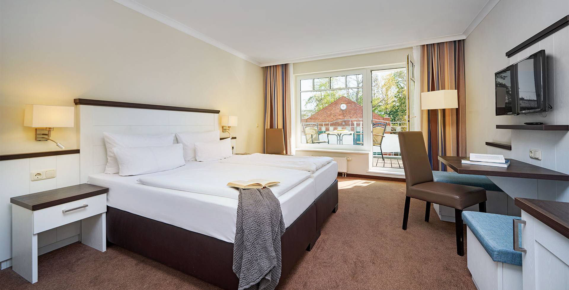 Economy Doppelzimmer im Strandhotel Luise mit Bett, Schreibtisch, TV, Stuhl und großem Fenster.