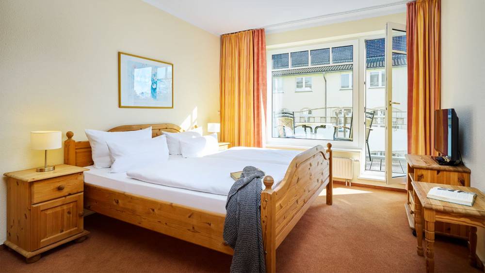 Helles Schlafzimmer mit Doppelbett, Nachttischen, Fernseher und Zugang zum Balkon im Strandhotel Luise in Zinnowitz.