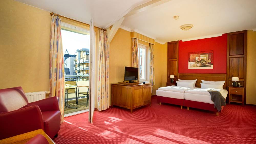 Doppelzimmer Landseite in der Strandvilla Viktoria auf Usedom mit Balkonzugang, zwei Betten, Sessel, TV und hellem Tageslicht.