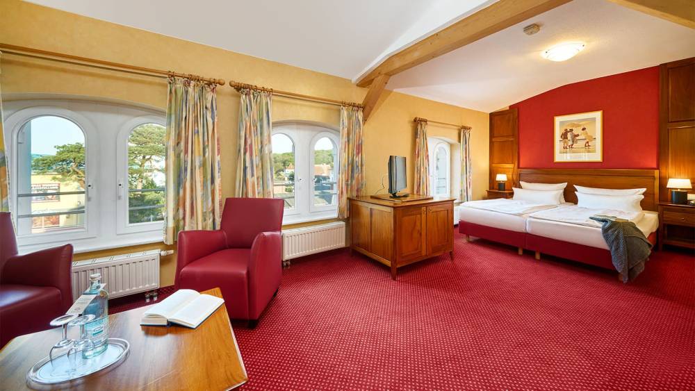 Doppelzimmer Promenade in der Strandvilla Viktoria mit Rundbogenfenstern, Sesseln, Teppich und klassischem Holzmobiliar.