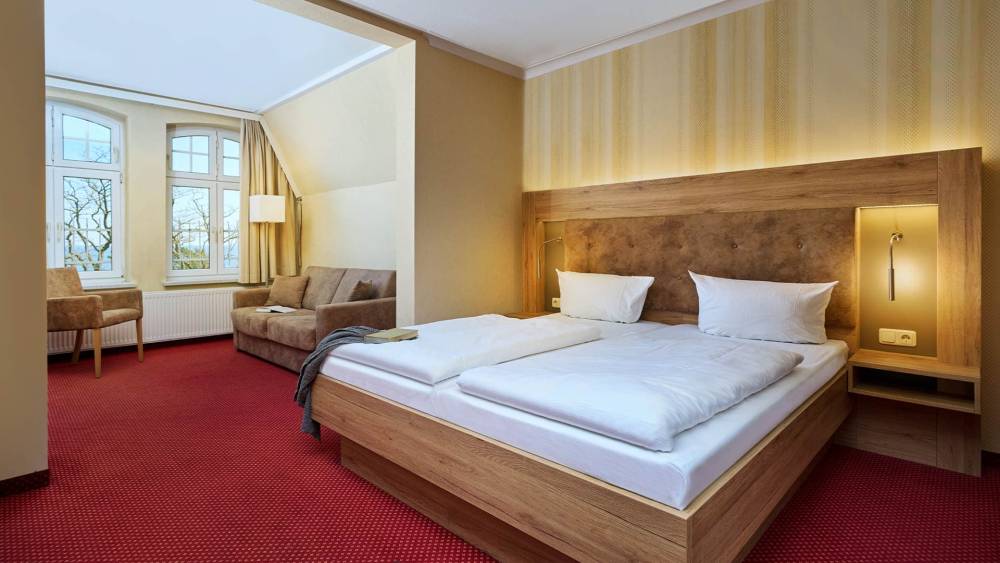 Gemütliches Doppelzimmer mit Sitzbereich und großen Fenstern im Strandhotel Garni Kormoran an der Ostsee.