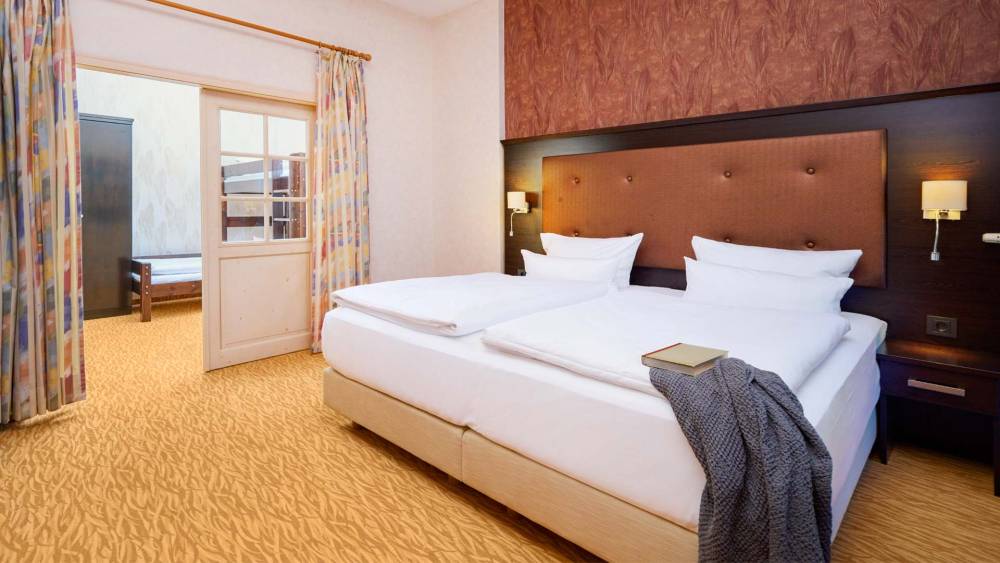 Doppelbett mit Nachttischen, Lampen und Blick ins Kinderzimmer der Family Suite im Hotel Preußenhof.