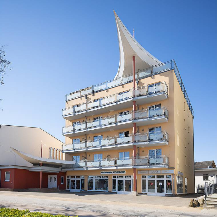 Das Strandhotel Prinz von Preußen mit gelber Fassade, Balkonen und Geschäften im Erdgeschoss unter blauem Himmel.