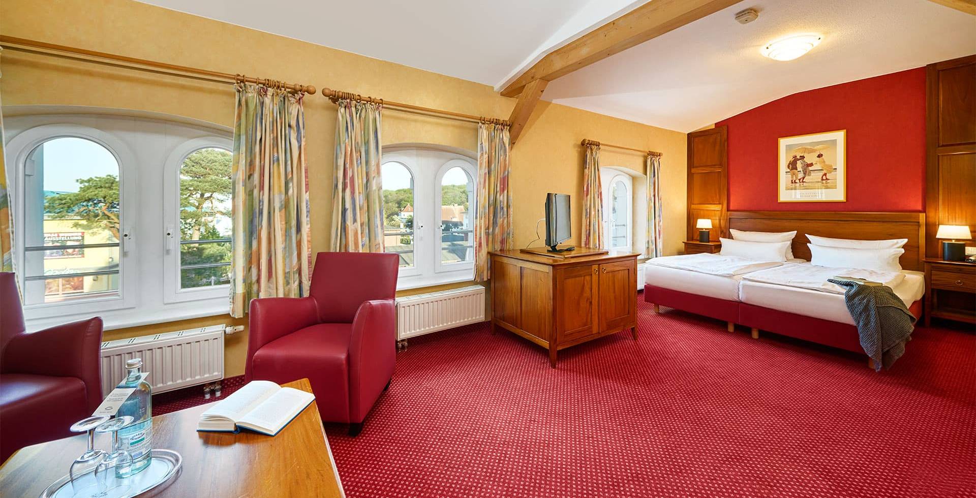 Doppelzimmer Promenade in der Strandvilla Viktoria mit Rundbogenfenstern, Sesseln, Teppich und klassischem Holzmobiliar.