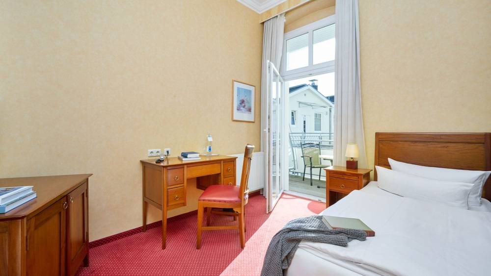 Einzelzimmer Landseite in der Strandvilla Viktoria mit klassischem Holzmobiliar, Tageslicht und Zugang zum Balkon.