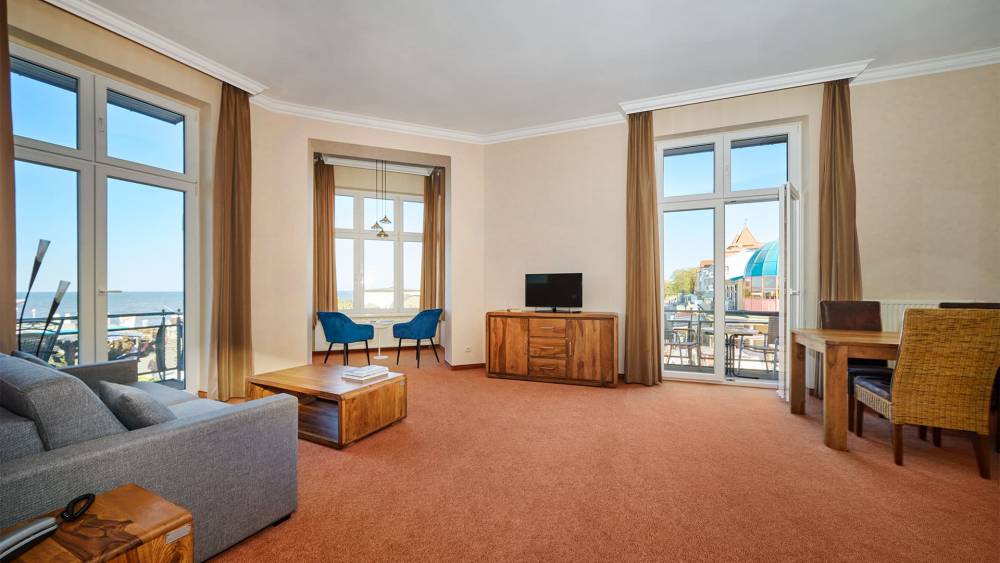 Turm Suite im Strandhotel Preußenhof mit Sofa, TV, Balkon, Sesseln und großem Fenster zur Ostsee.