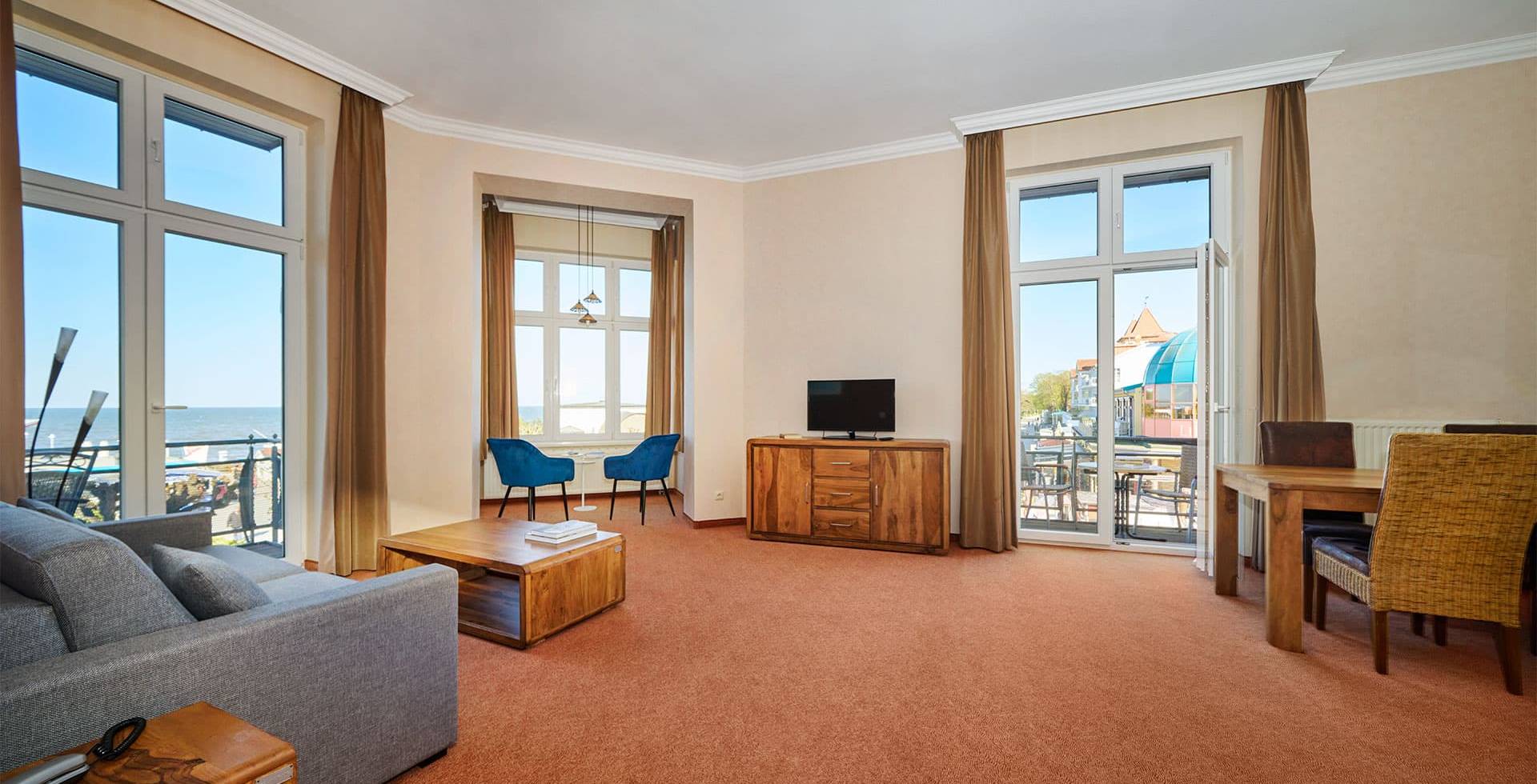 Turm Suite im Strandhotel Preußenhof mit Sofa, TV, Balkon, Sesseln und großem Fenster zur Ostsee.