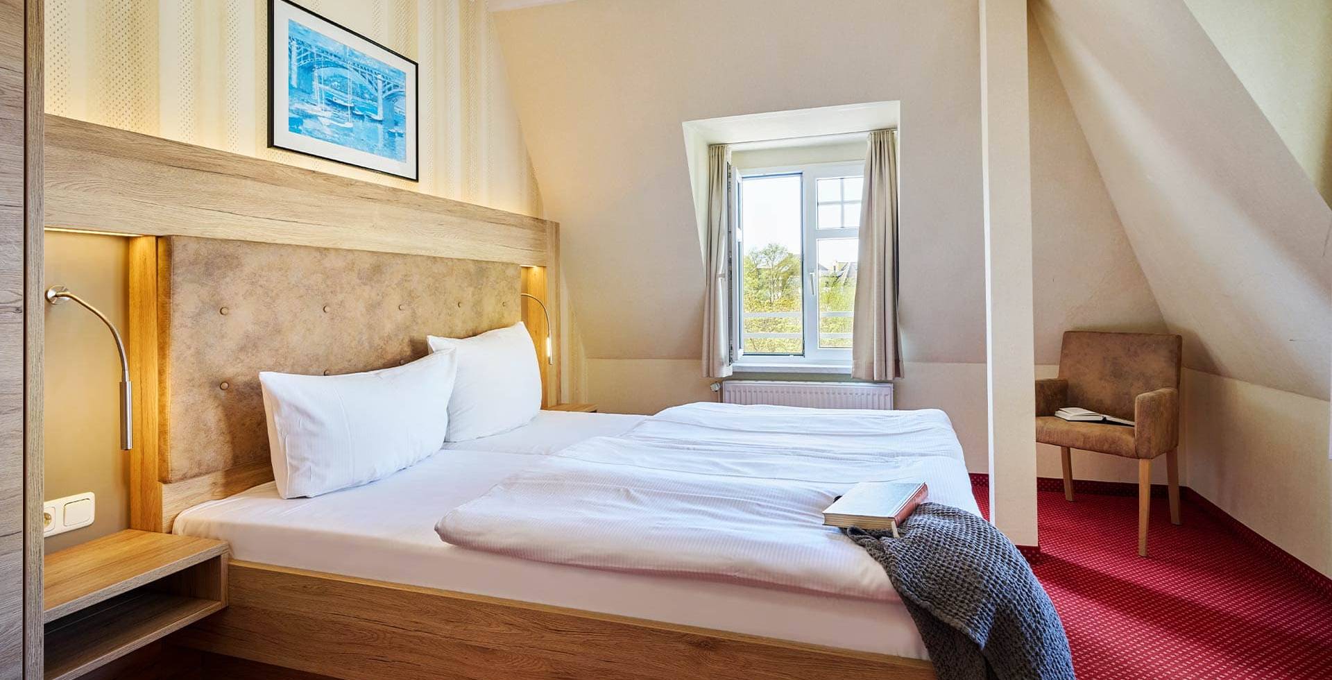 Großzügiges Doppelzimmer mit Sessel, Bett und Fenster im Strandhotel Kormoran auf Usedom.