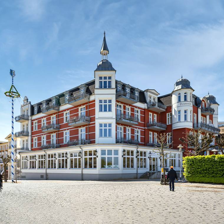 Imposantes Strand- und Wellnesshotel Preußenhof mit roten und weißen Fassaden, Balkonen und Türmen unter blauem Himmel.