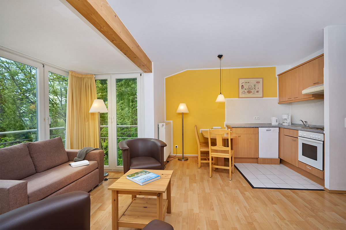 Modern gestalteter Wohn- und Essbereich der Ferienwohnung Strandperle mit braunen Möbeln und warmen gelben Wänden.
