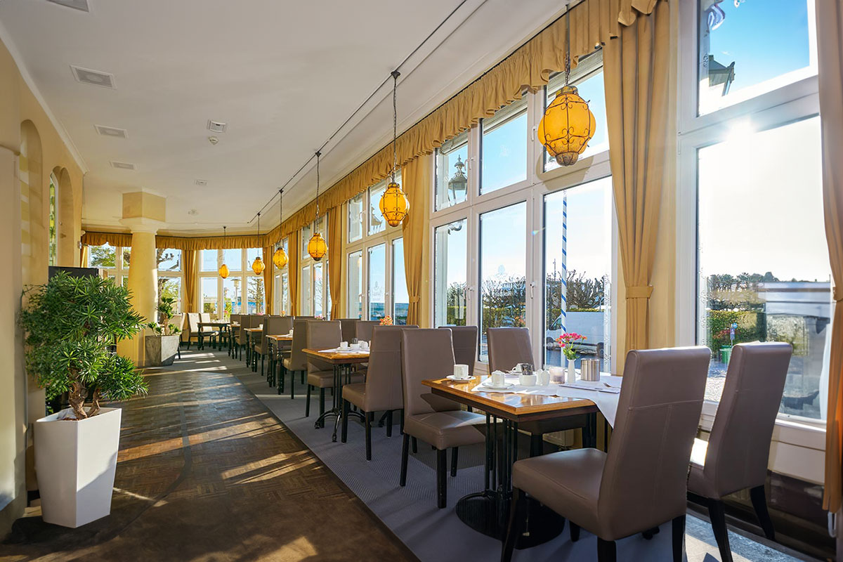 Helles Restaurant mit Panoramafenstern, gelben Vorhängen und gemütlich gedeckten Tischen von Schoener Inseln auf Usedom.